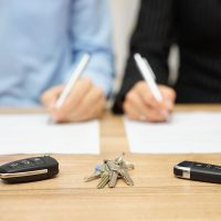property-division-fedor-sm Two individuals signing documents related to property division, with car keys and house keys on a table, symbolizing family law and divorce proceedings.
