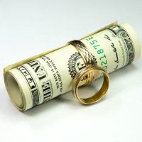 spousal-support-kozlov-sm Roll of cash with a gold wedding ring, symbolizing financial assets and spousal support in divorce proceedings.