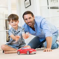 FedorKozlov_1_FactorsInfluencingtheParentingTimeSchedule-sm Father and son playing together with a toy car, illustrating positive parenting time and family bonding in a home setting.