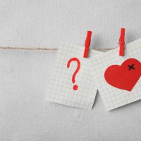 Question mark and broken heart illustrations on paper notes, symbolizing uncertainty and emotional struggles in marriage, relevant to divorce considerations.