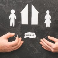 property division Hands holding wedding rings with paper cutouts of a man and woman, two houses, and the word "DIVORCE," symbolizing property division in Illinois divorces.